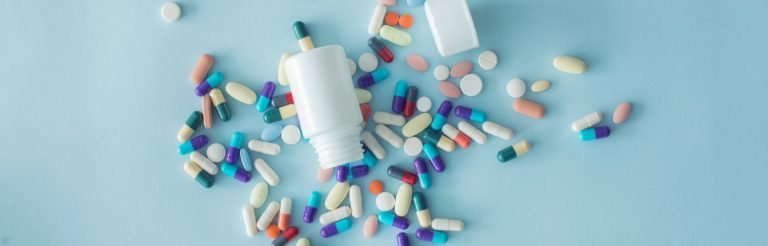 Multi-colored pills spilling out of a bottle on a blue background