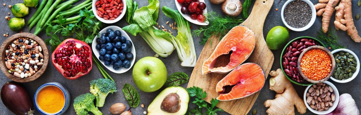 A spread of healthy foods including salmon, apples, berries, nuts and green vegetables.