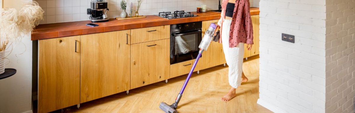 A woman vacuuming a laminate floor in her kitchen.