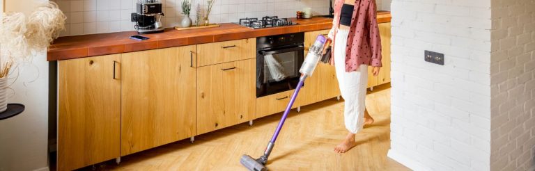 A woman vacuuming a laminate floor in her kitchen.