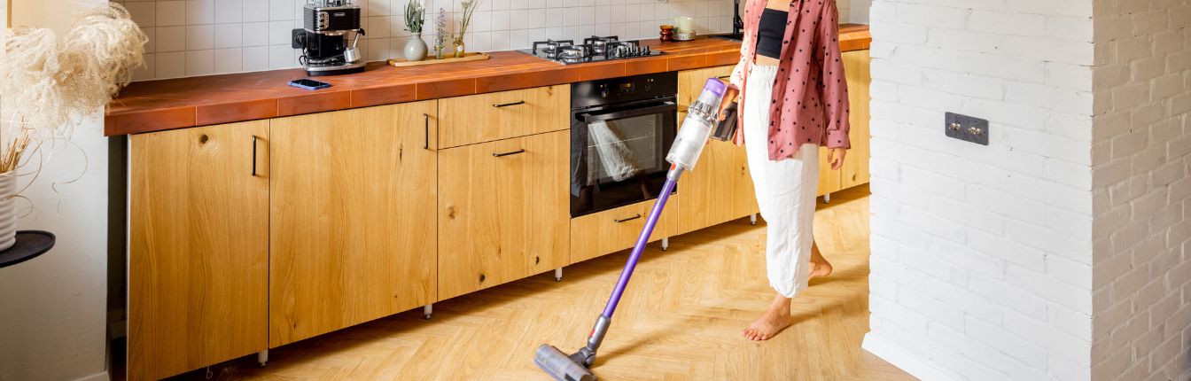 A woman vacuuming a laminate floor in her kitchen.