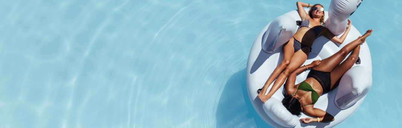 Two women on an inflatable swan floating in a pool.