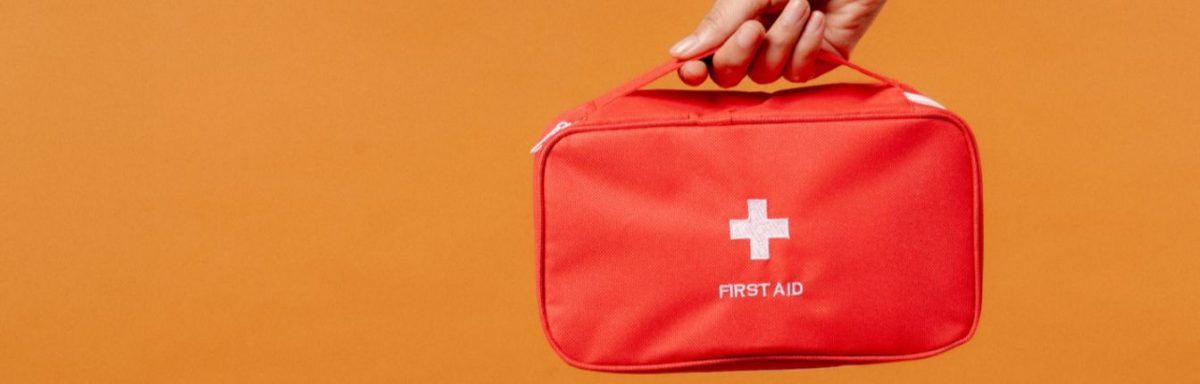 A red first aid kit being held against an orange background.