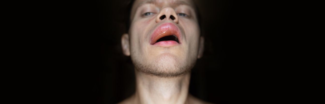 A man's face with very swollen lips, against a black background.